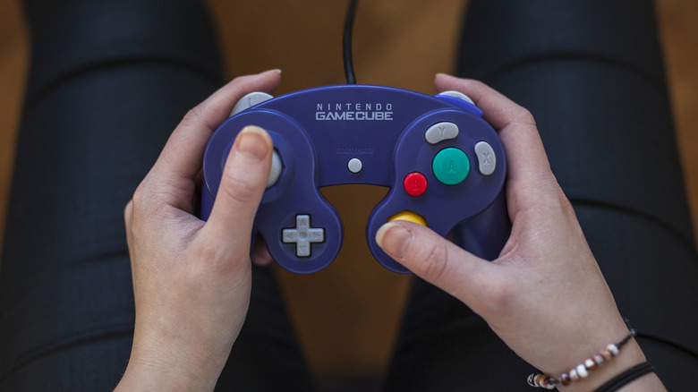 Hands holding a purple Nintendo GameCube controller while pressing the analog stick and buttons.