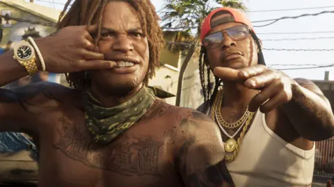 Rockstar Games Two characters from GTA 6 gesture at the viewer. One, wearing a heavy gold watch, pulls back his top lip to reveal teeth covered in gold. The man next to him wears three thick, gold chains, one with a large round medallion attached. Both are heavily tattooed. The image is convincingly lifelike despite being computer generated
