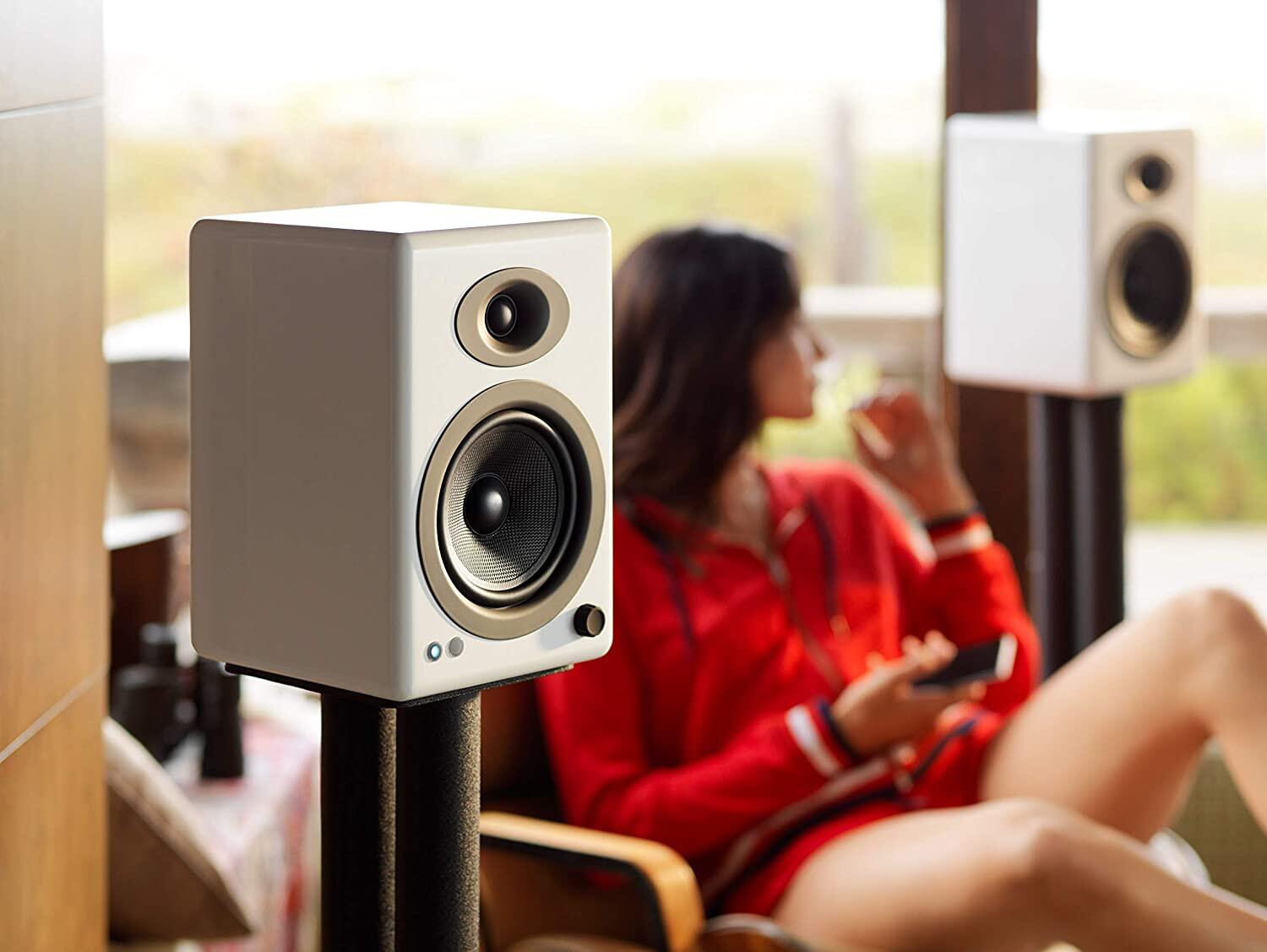 The white AudioEngine A5 Plus Wireless speakers flanking a woman in red watching television.