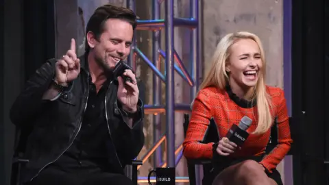 Getty Images Hayden Panettiere sitting next to Charles Esten, both holding microphones at a Q&A event and laughing heartily