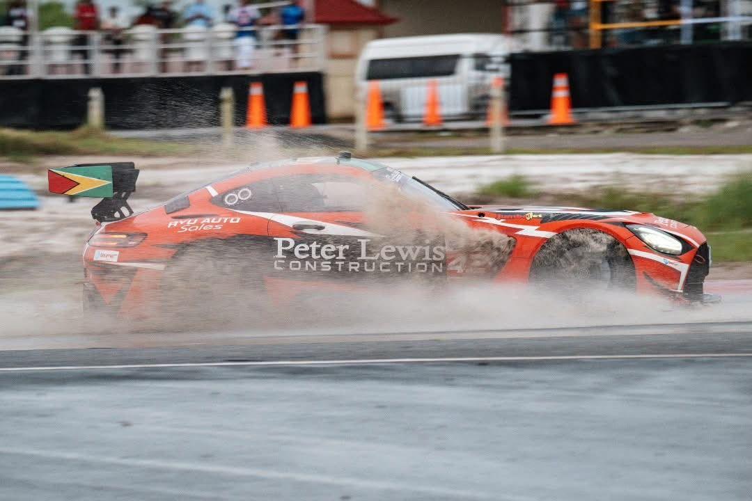 A red and black Mercedes driving on a wet race track with muddy water spraying out from underneath the car.