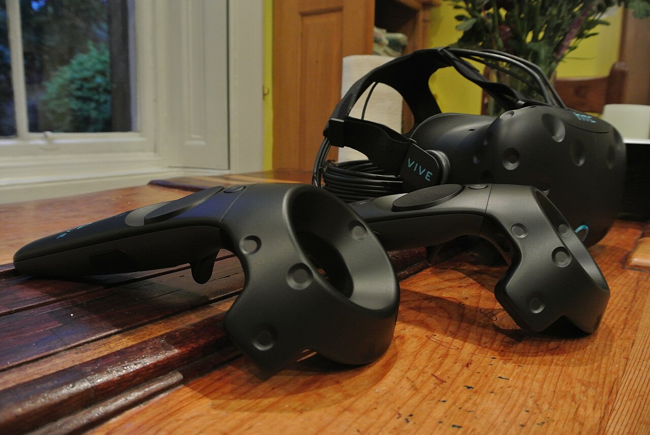 An HTC Vive headset and two wand controllers resting on a wooden table