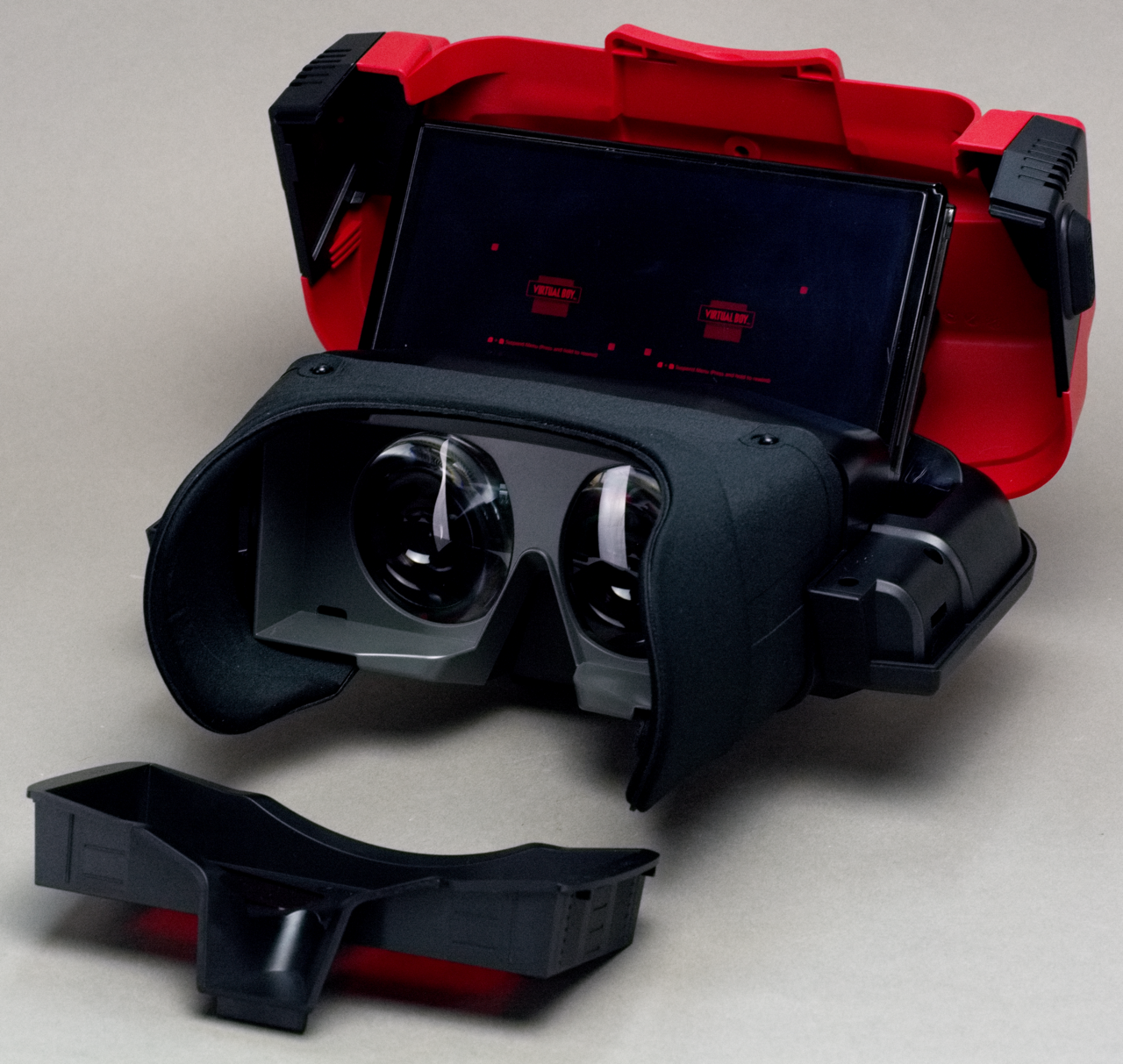 The Nintendo Switch Virtual Boy accessory taken apart, showing a Switch console seated inside the red shell running the Virtual Boy app in red on black
