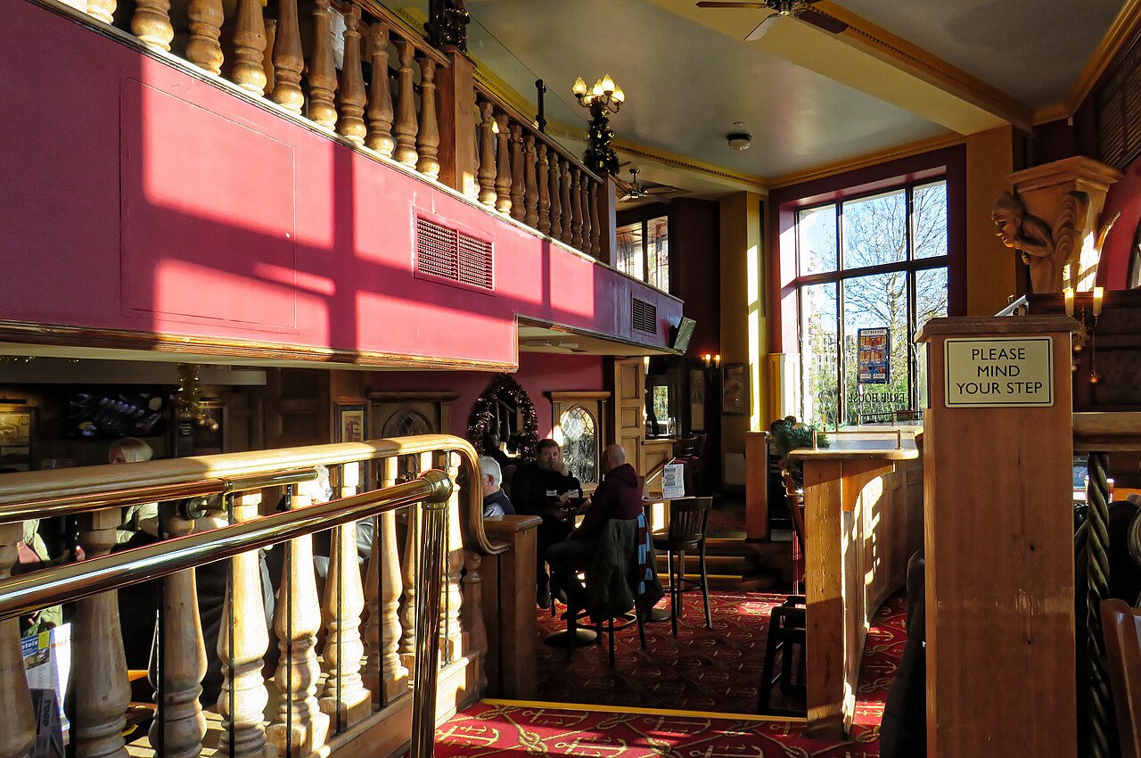 Interior of a JD Wetherspoon pub in London with wooden balustrades and patterned carpet