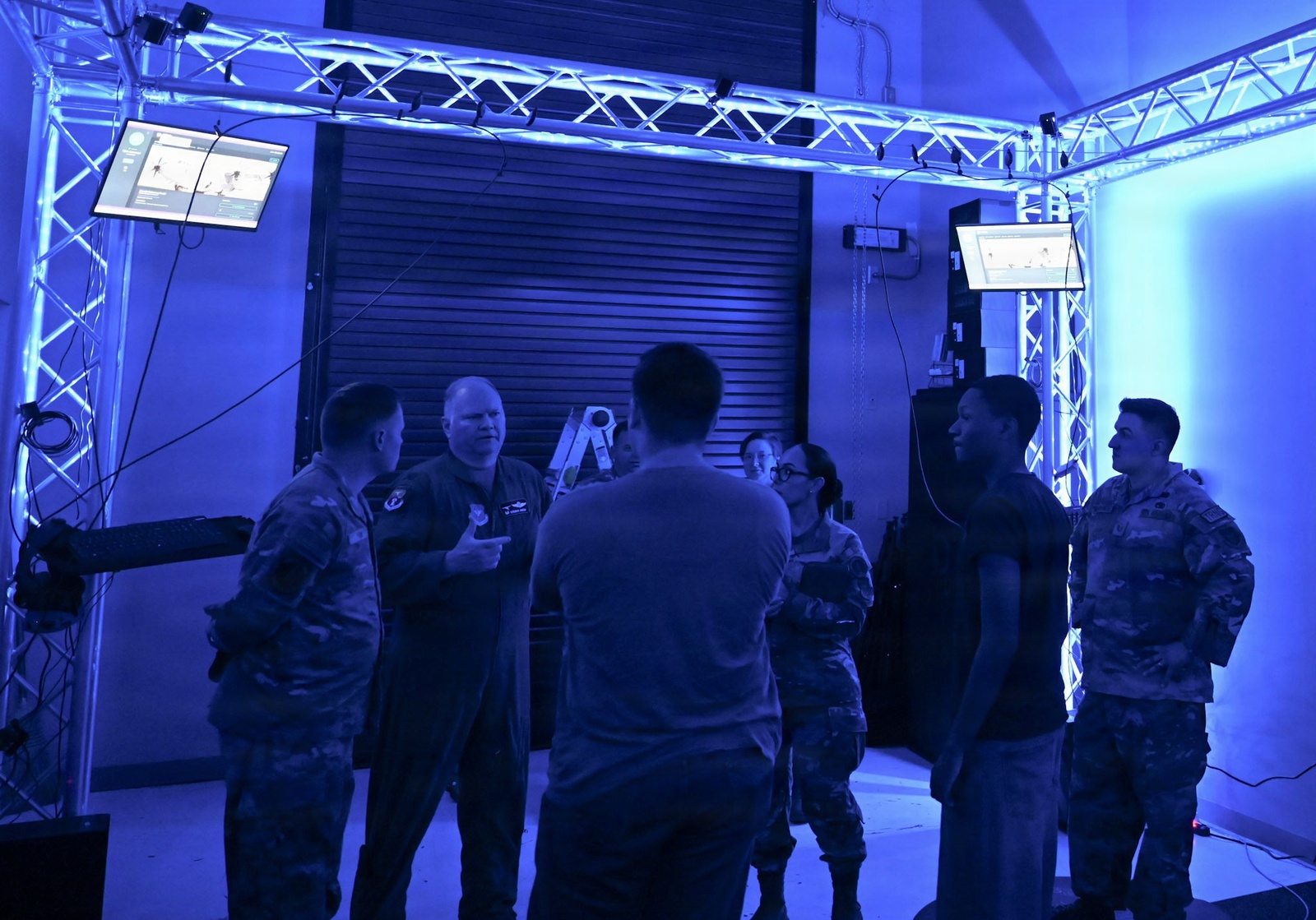 Airmen gathered inside the 913th Airlift Group Virtual Reality Training Center, a converted storage bay lit in blue with overhead truss and wall-mounted monitors