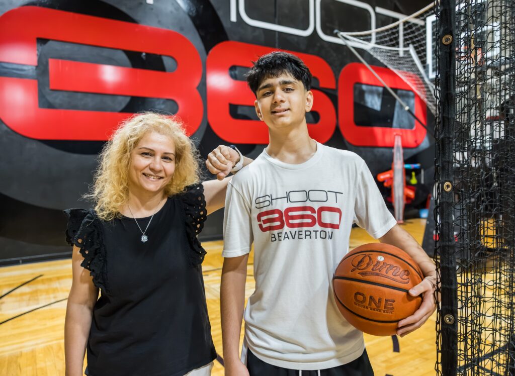 A teenage boy holding a basketball stands next to his mom.