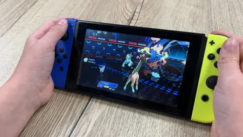 Darren Rozier/BBC A boy playing a Pokemon video game on a handheld Nintendo Switch console. The console has one blue end and one yellow end with a screen in between.