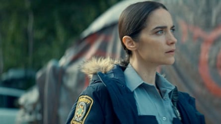 A woman with brown hair in a police uniform looks into the distance