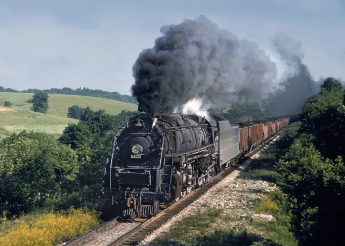 A colored image of a locomotive steam train barreling down the tracks. There is black smoke blowing out of the front of the train.
