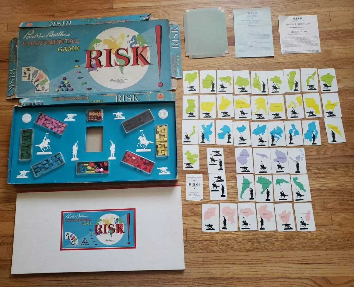 Vintage Risk board game set on a wooden surface. Includes the game box, board, cards, instructions, and various colored pieces. The box features a world map design. The pieces are organized by type.