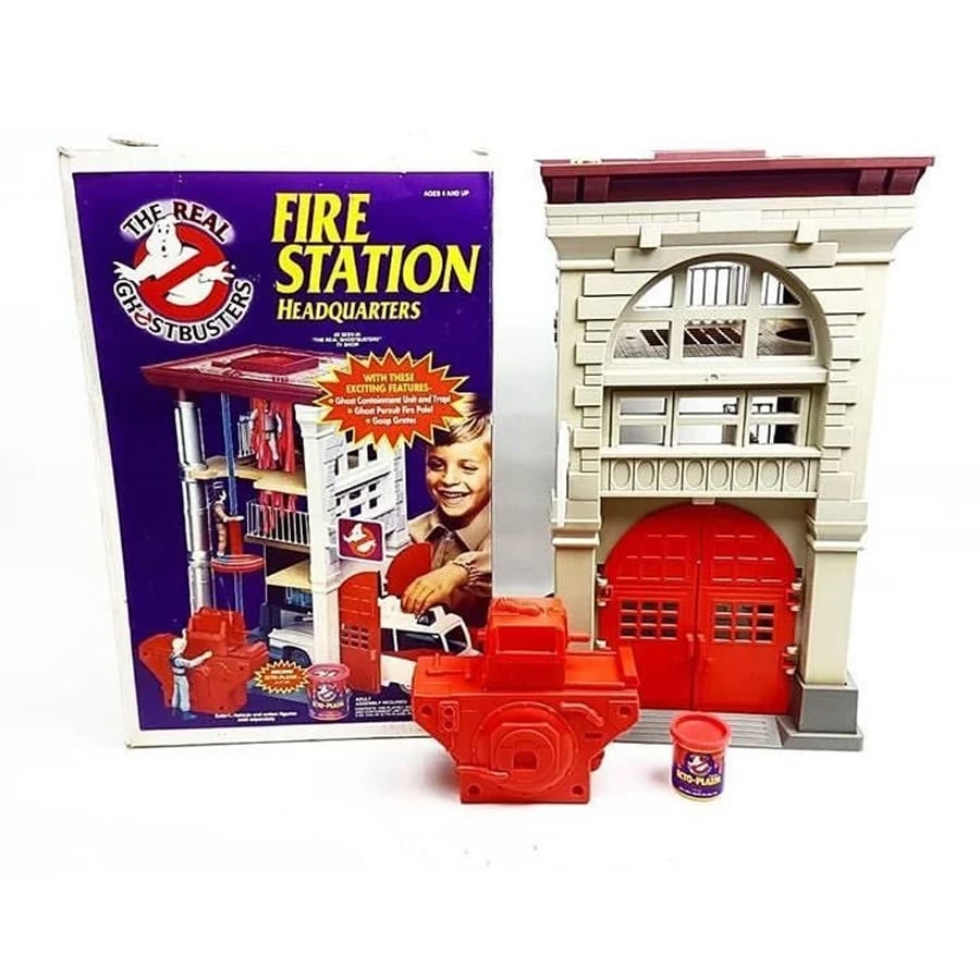 The Real Ghostbusters Fire Station Headquarters playset with box, toy firehouse, red ghost trap accessory, and small canister, all displayed on a white background.