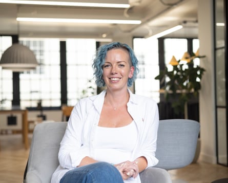a smiling woman with blue hair sitting in an open plan office