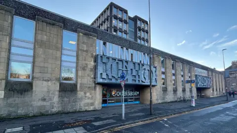 A general view of the rear of Argyle House. The building is low and is made of light stone with dark motifs above the door and windows to the left side.