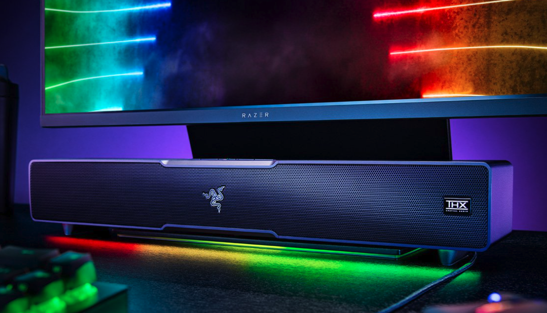 The Razer Leviathan V2 lit up in rainbow colors placed below a computer monitor.