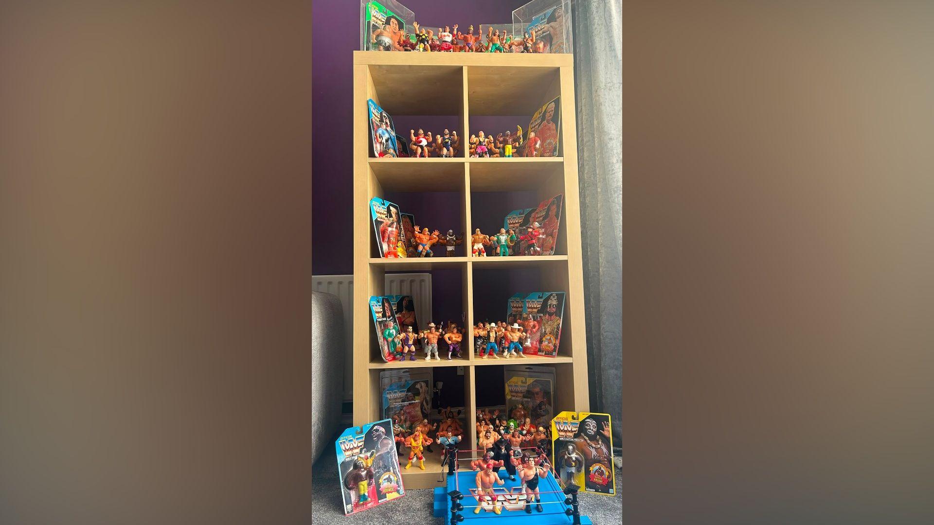 A shelving unit filled with wrestling figures. Some are in their packaging and on the floor is a blue wrestling ring with several figures standing in it