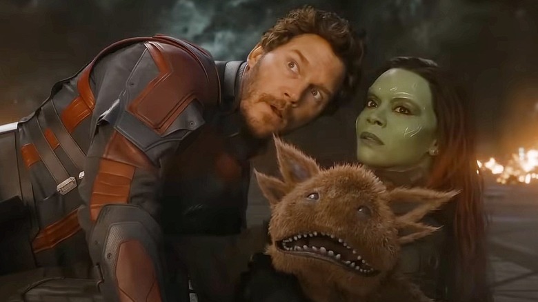 Chris Pratt as Peter Quill/Star-Lord and Zoe Saldaña as Gamora in Guardians of the Galaxy Vol. 3, crouched next to each other with a space alien creature between them.