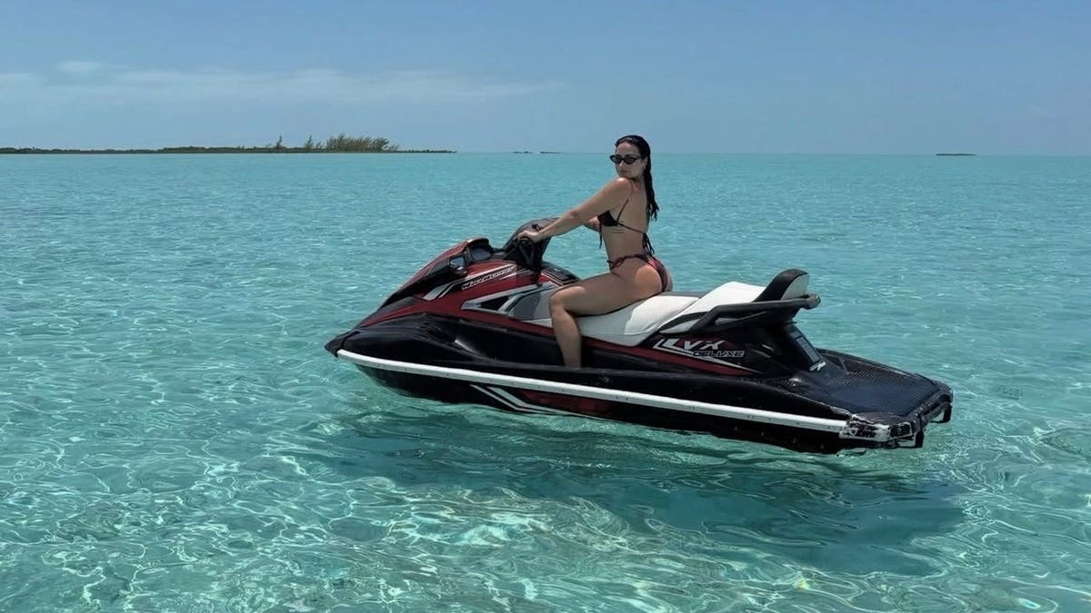 Demi Lovato poses on a red jet ski in a colorful string bikini and dark sunglasses during a Bahamas getaway.