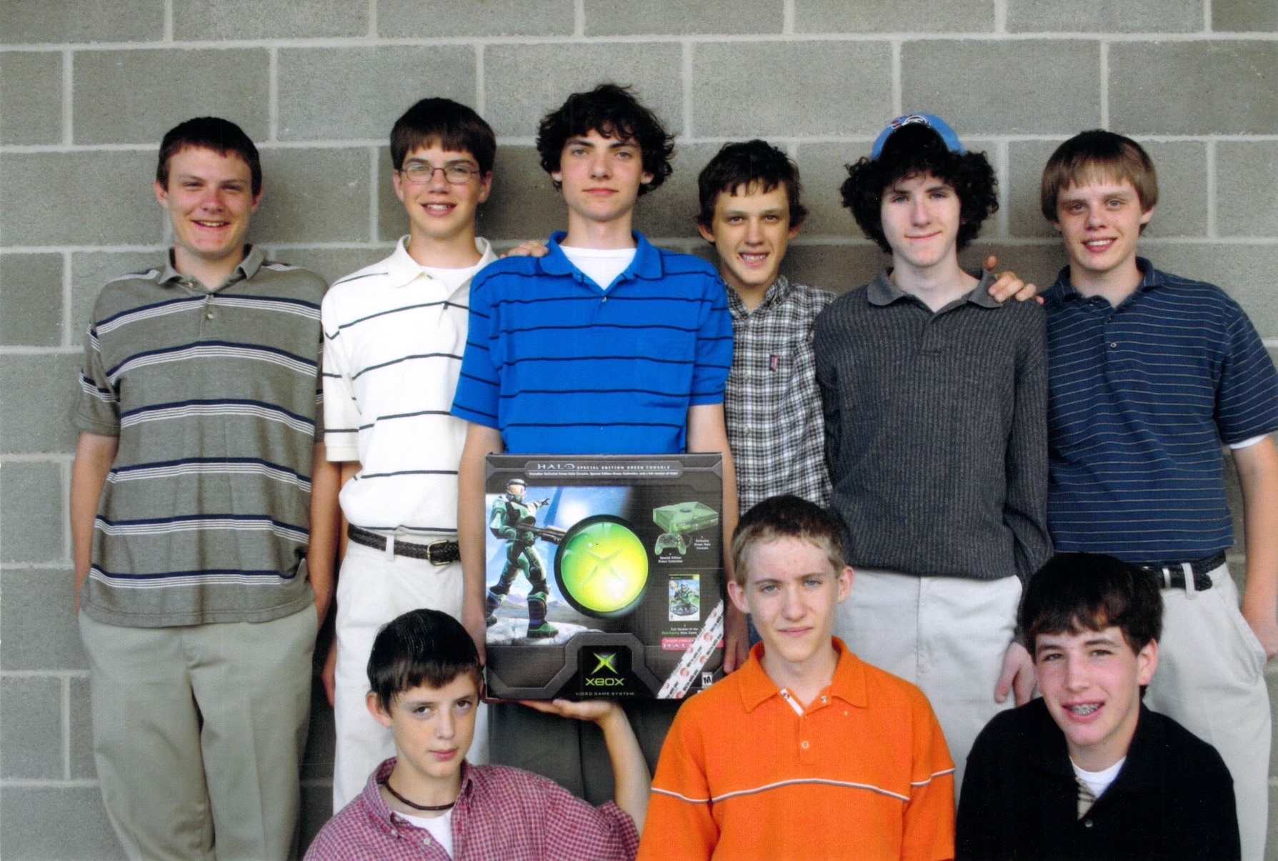 A group of 9 boys with someone holding up a box of the original Xbox containing a copy of Halo: Combat Evolved.