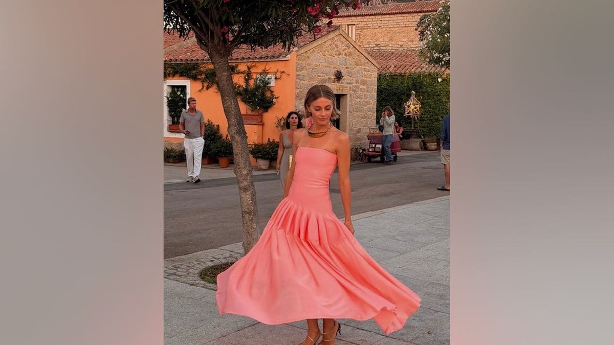 Julianne Hough poses outdoors in Sardinia wearing a strapless coral-pink gown with a flowing skirt.