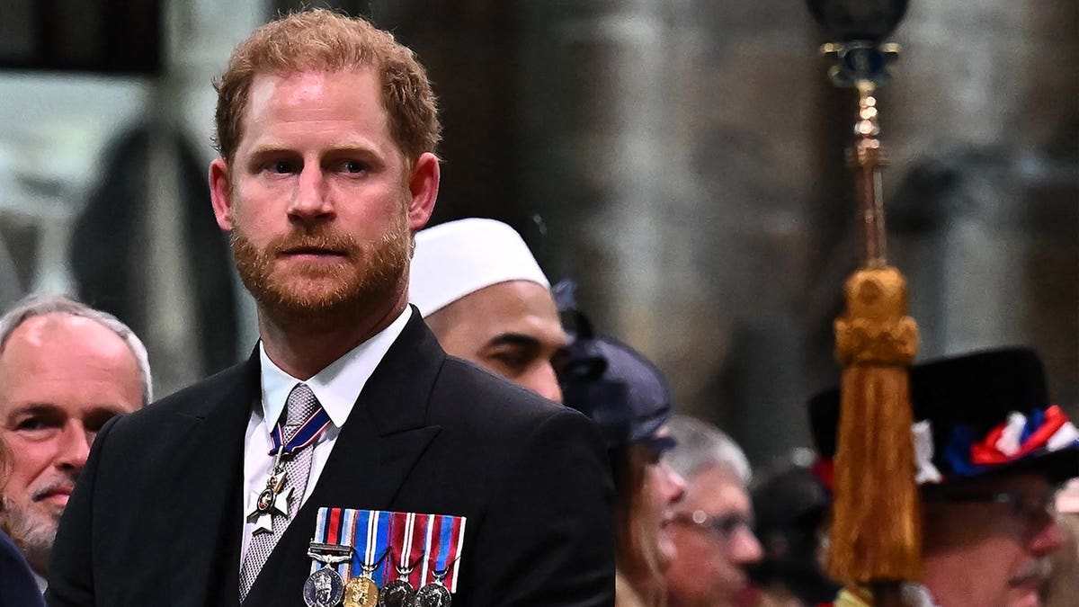 Prince Harry in a dark suit and medals looking up during his father's coronation ceremony.