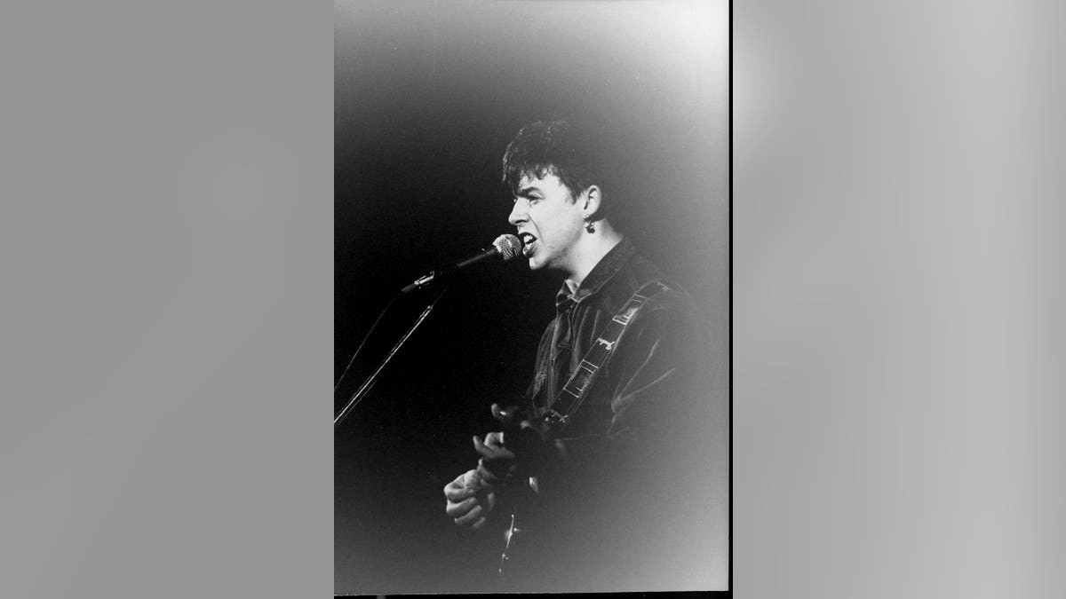 Roland Orzabal performing on stage and singing to a mic.