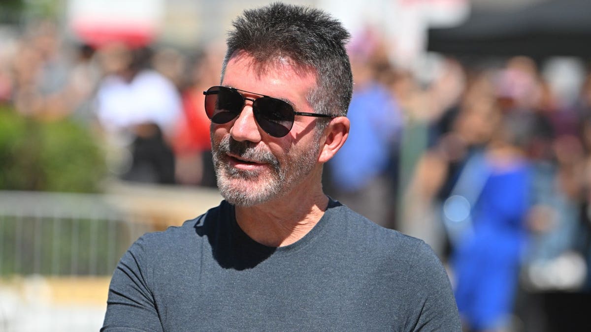 Simon Cowell wears black sunglasses and a dark gray T-shirt at an outdoor event