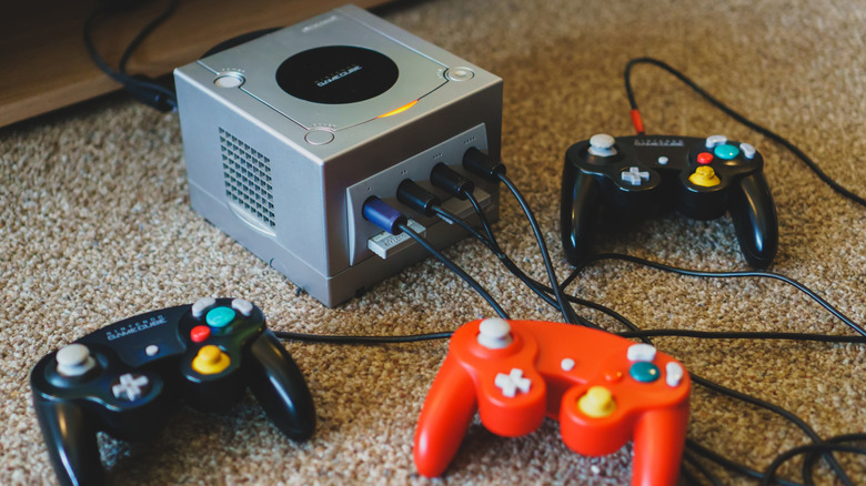 A GameCube console on the ground surrounded by several controllers