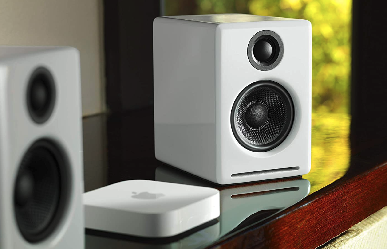 The white AudioEngine A2 speakers on top of a reflective wooden surface, complete with Apple TV.