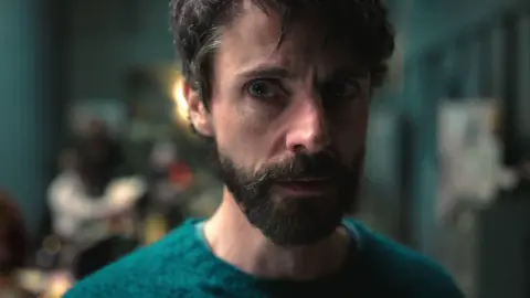 Netflix Close-up of Matthew Goode who is wearing a green jumper and is staring off to the right of the camera.