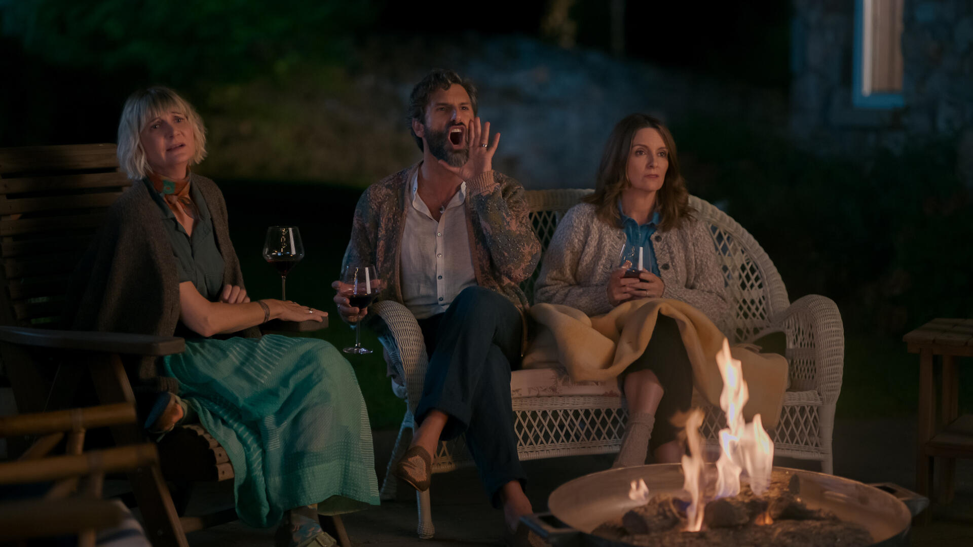 A man and two women sit next to a fire pit