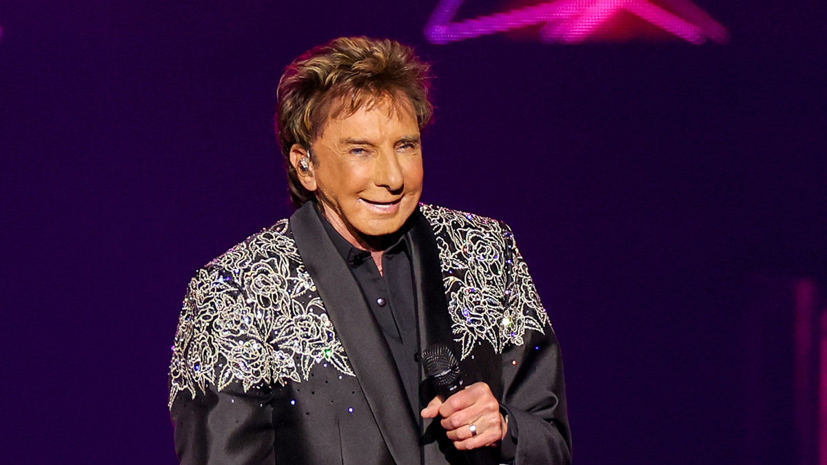 Barry Manilow holds a microphone on stage.