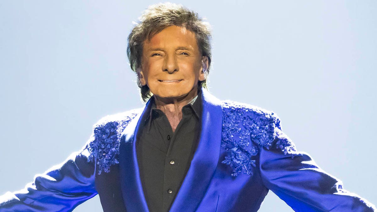 Barry Manilow smiles on stage with his arms outstretched.