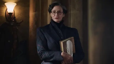 Lara Cornell/HBO Janet McTeer in a checked jacket holding a book and white feather