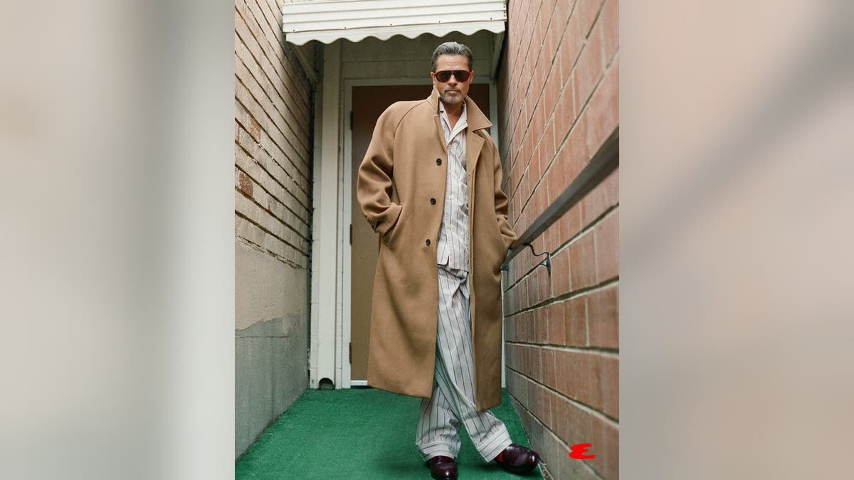 Brad Pitt stands outside wearing sunglasses and a coat.