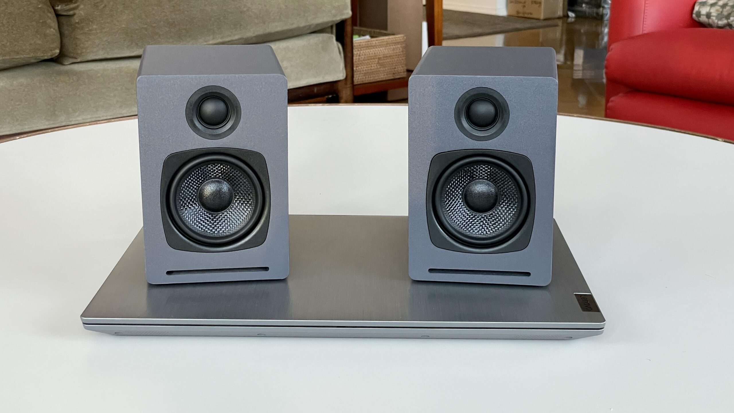 The dark grey AudioEngine One speakers resting on a silver computer on a living room coffee table.