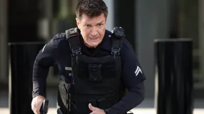 Officer Nolan, played by Nathan Fillion, moves in tactical gear with gun drawn in a tense scene from The Rookie.