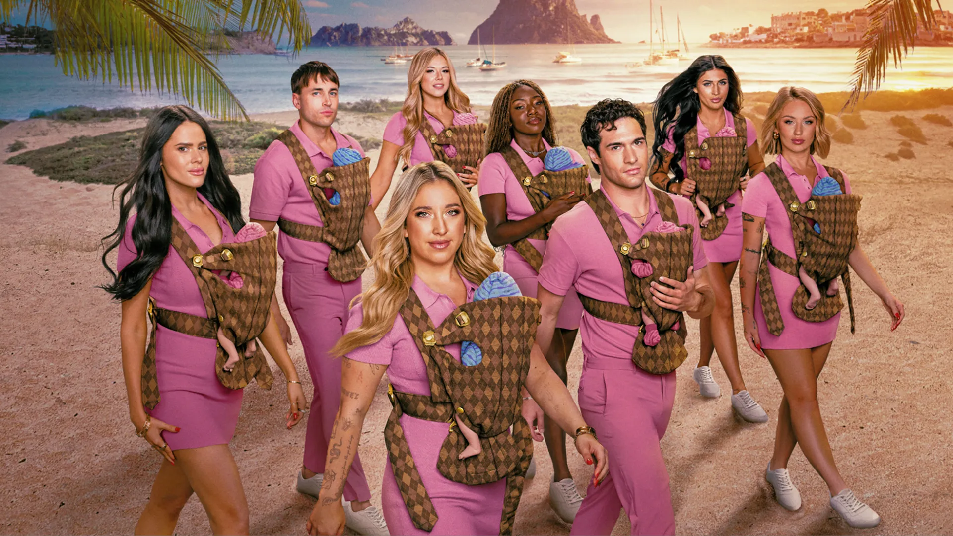 A group of eight people dressed in matching pink outfits walk along a sandy beach at sunset while wearing patterned baby carriers containing dolls.