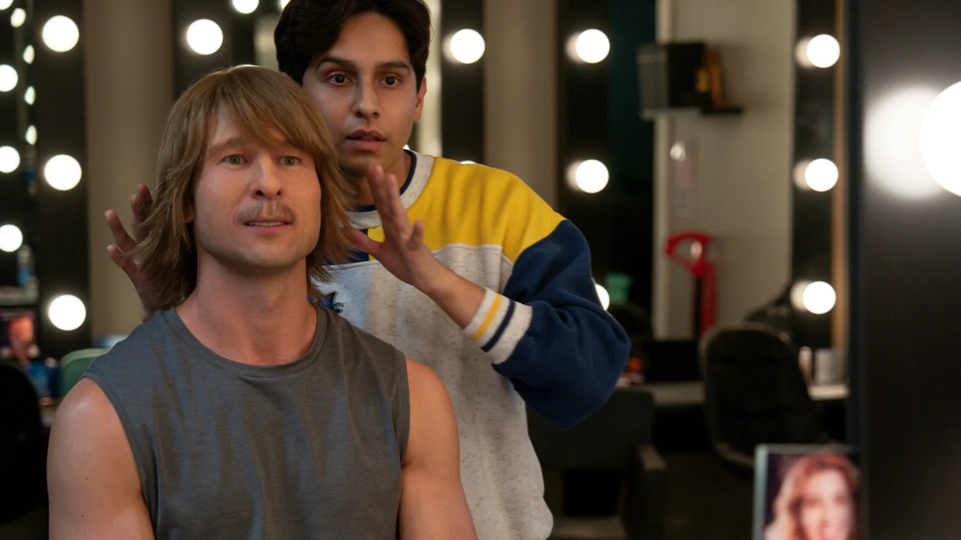 Russ Holliday (Glen Powell) in chair and makeup transforms into his Chad Powers persona with Danny's help (Frankie Rodriguez).