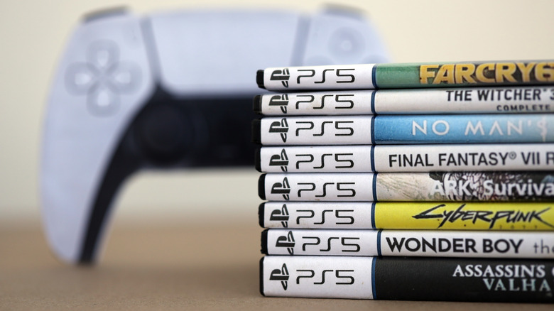 A stack of PS5 game boxes next to a PS5 controller.