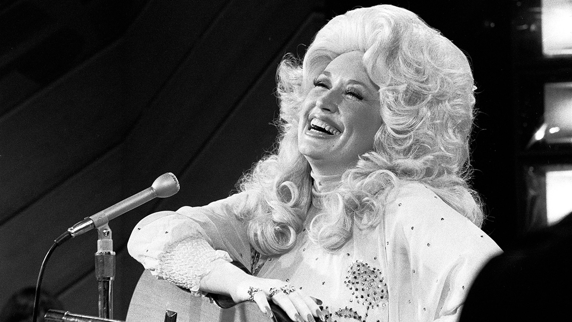 Dally Parton laughing on stage in 1976.