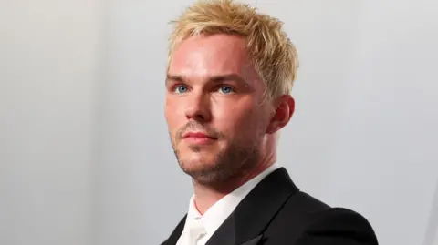 Getty Images Nicholas Hoult looking slightly off camera with dyed blond hair, white shirt and tie and black dinner jacket at the 2026 Vanity Fair Oscar Party held at the Los Angeles County Museum of Art