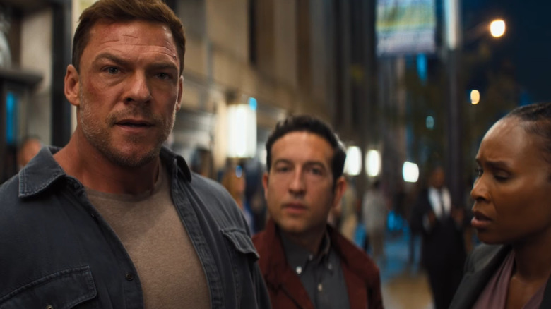 Alan Ritchson as Jack Reacher standing on a busy street next to Chris Marquette as Jacob Merrick and Sydelle Noel as Tamara Green in Reacher