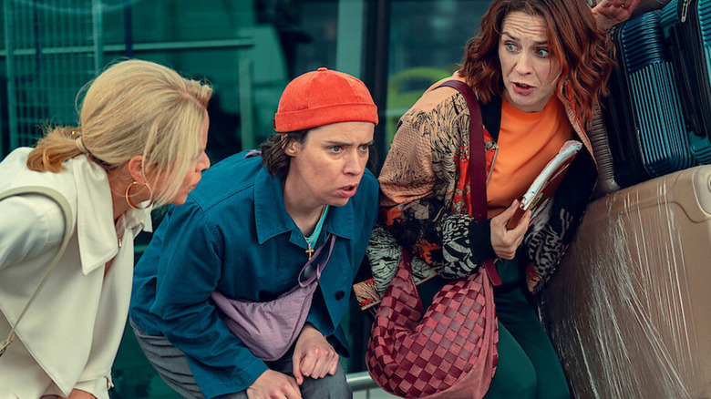 Robyn, Dara, and Saoirse (burdened by luggage) crouching in alarm outside of an airport