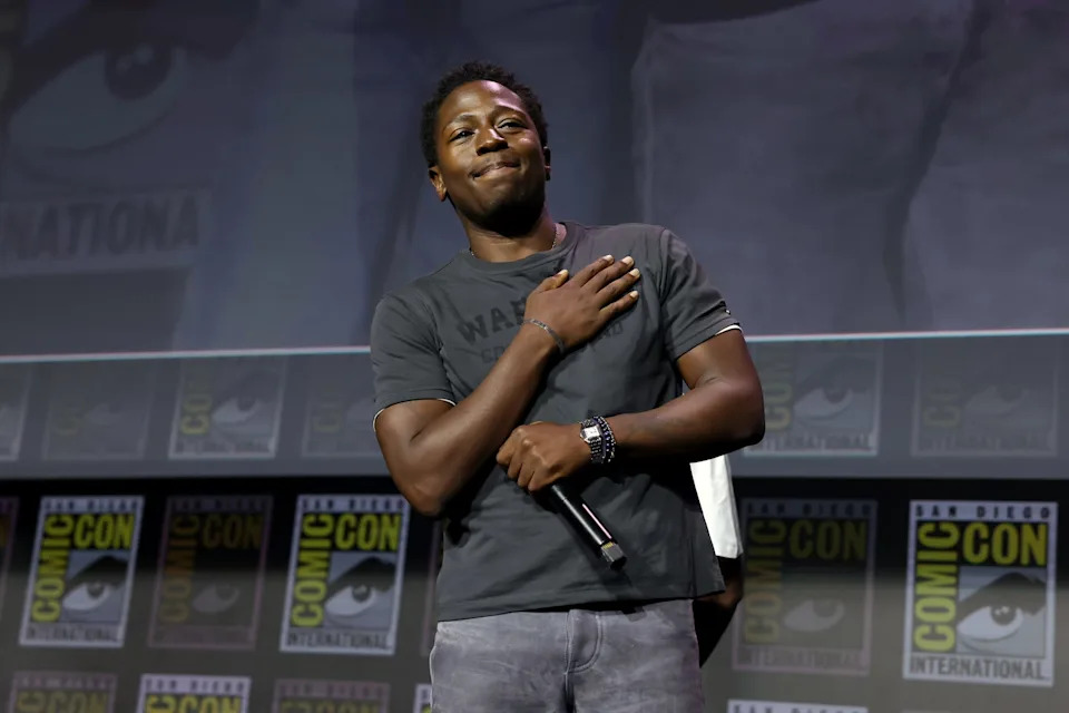 David Jonsson on stage at San Diego Comic-Con, holding a microphone, with Comic-Con logos in the background.