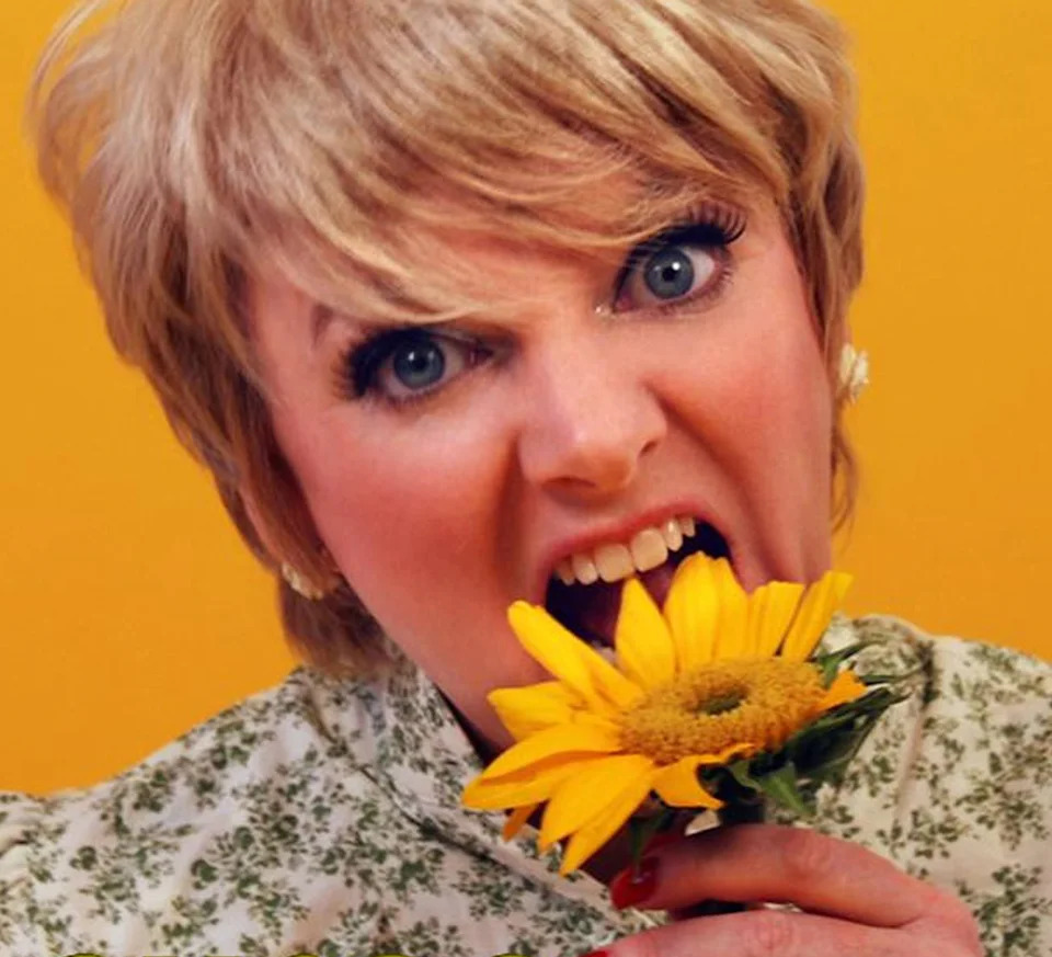 Alison Arngrim playfully bites a sunflower against a yellow background