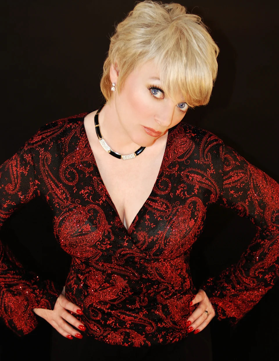 Alison Arngrim poses with hands on hips wearing a red and black paisley top