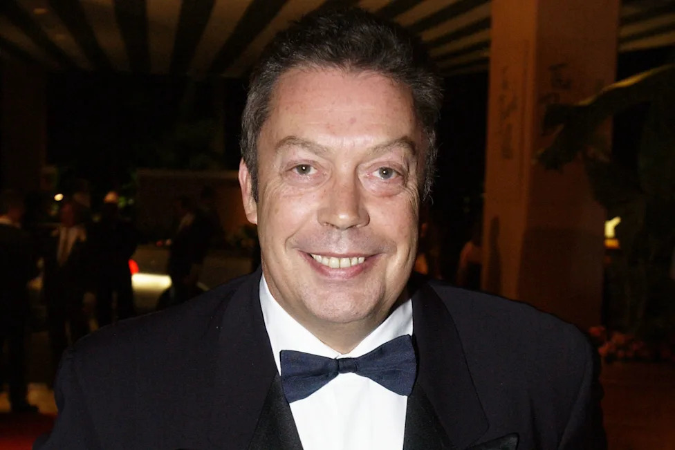A close up of Tim Curry smiling in a tuxedo