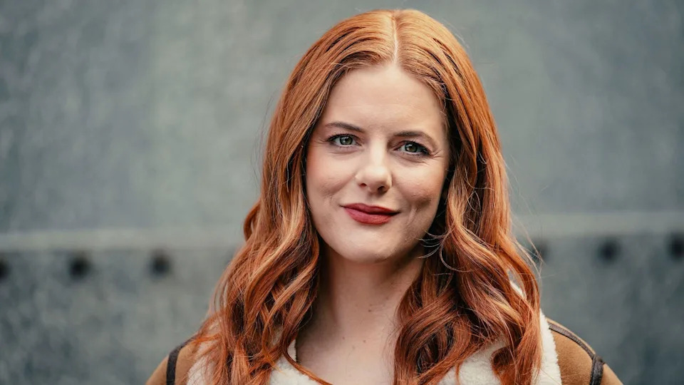 A red haired woman smiles at the camera