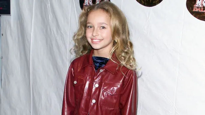 Panettiere pictured smiling at 11-years-old at a film premiere. She has curly dark blonde hair and wears a vinyl dark red jacket with a crused velvet blue top.