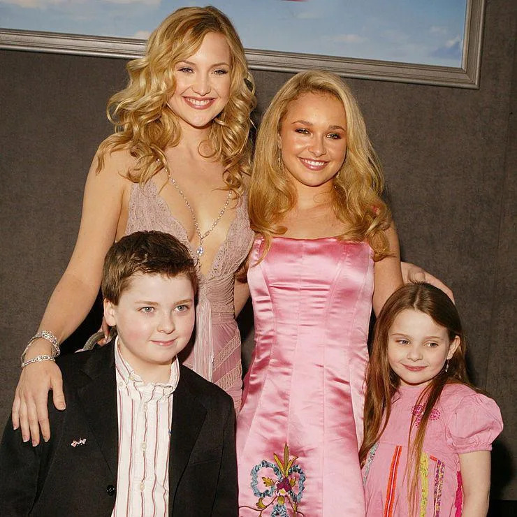 Panettiere is seen with curled blonde hair and wearing a pink silk mid-length dress as she smiles on the red carpet next to Kate Hudson in 2004. The pair have their arms around each other.